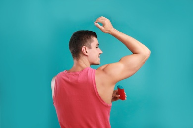 Photo of Young man applying deodorant to armpit on light blue background