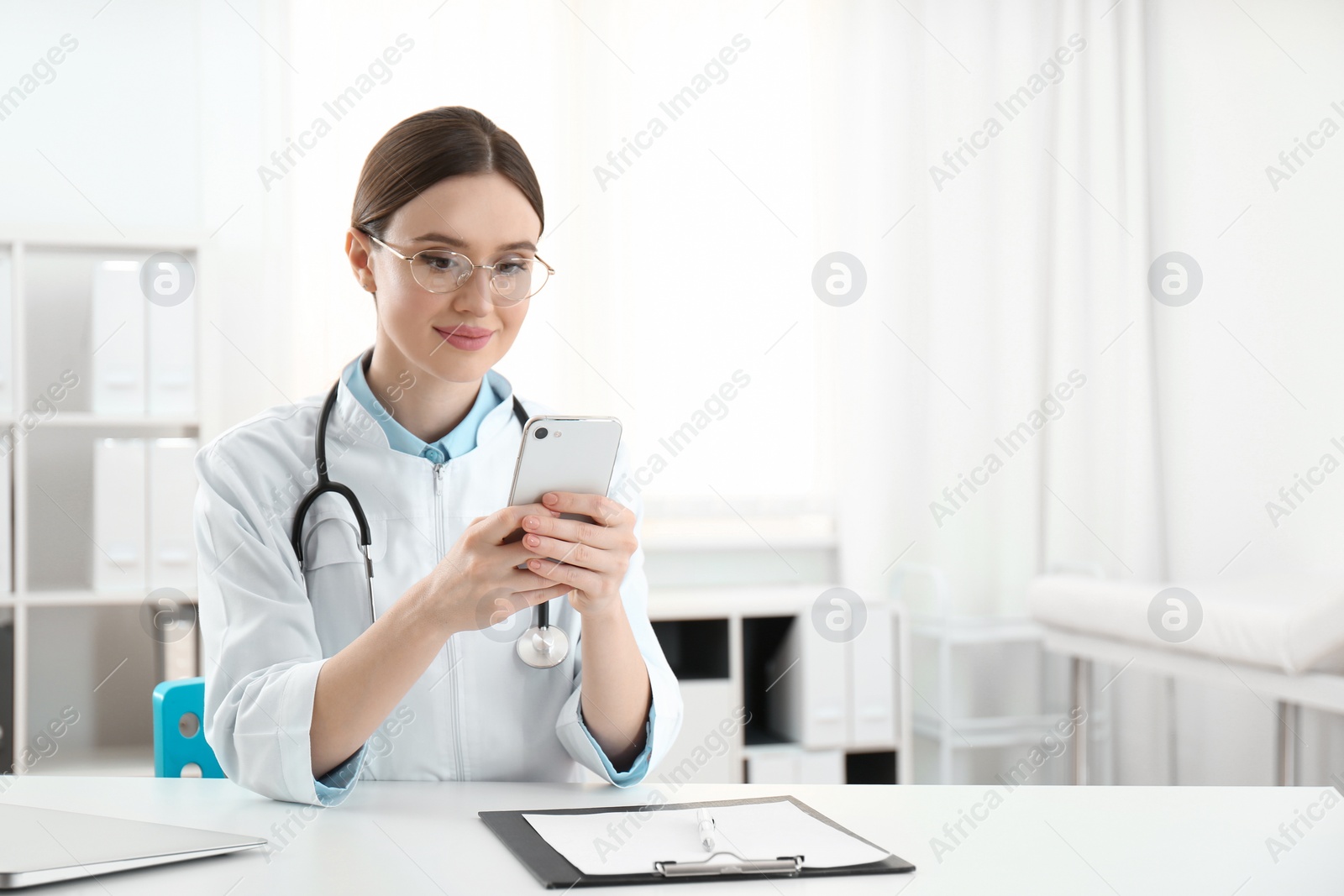 Photo of Young female doctor with smartphone at table in office