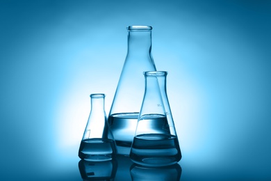 Conical flasks with liquid on table against color background. Laboratory analysis