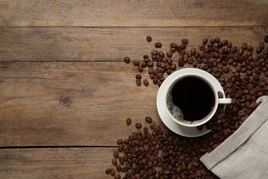 Cup of aromatic coffee and beans on wooden table, flat lay. Space for text