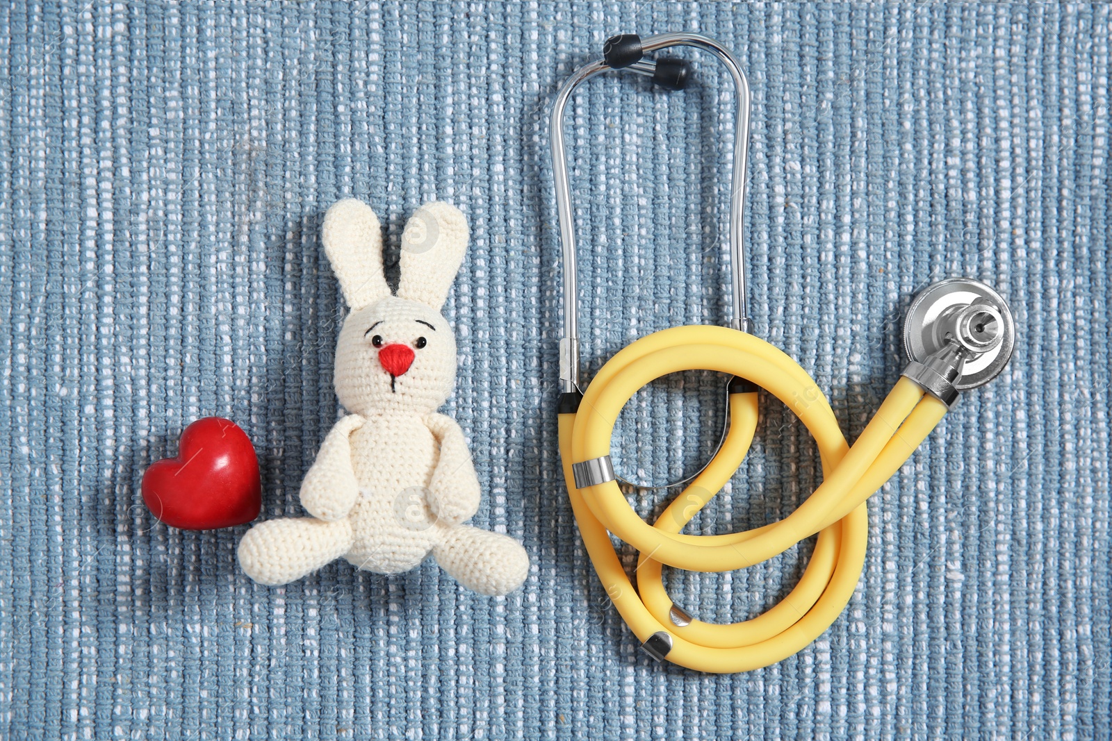 Photo of Flat lay composition with toy bunny, stethoscope and heart on fabric. Children's doctor