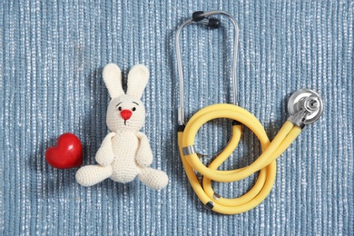 Flat lay composition with toy bunny, stethoscope and heart on fabric. Children's doctor