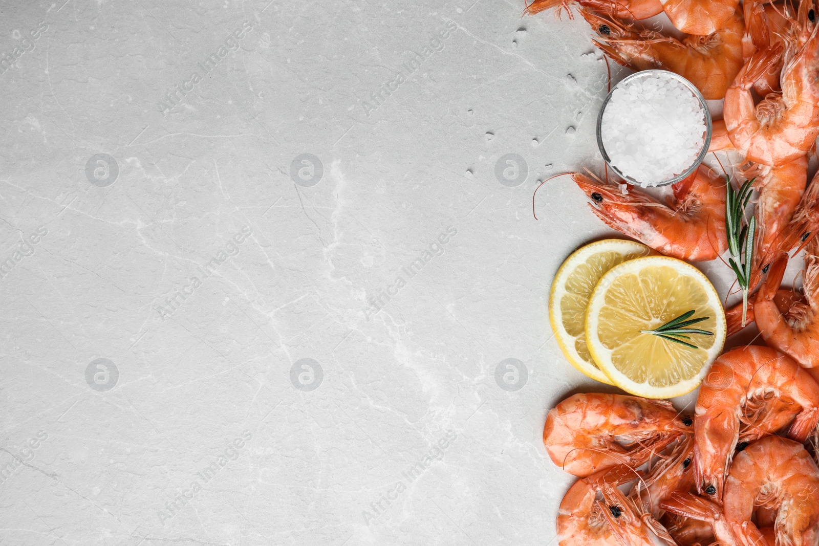 Photo of Delicious cooked shrimps with rosemary, salt and lemon on grey marble table, flat lay. Space for text