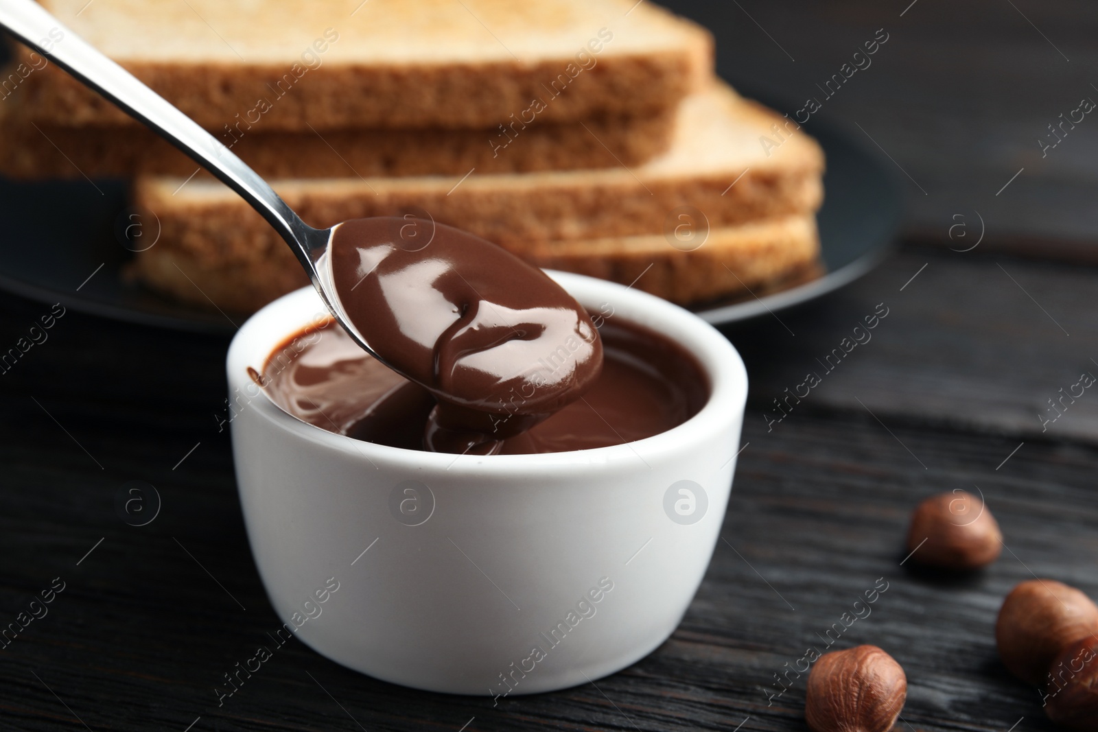 Photo of Spoon with tasty chocolate cream over bowl on table