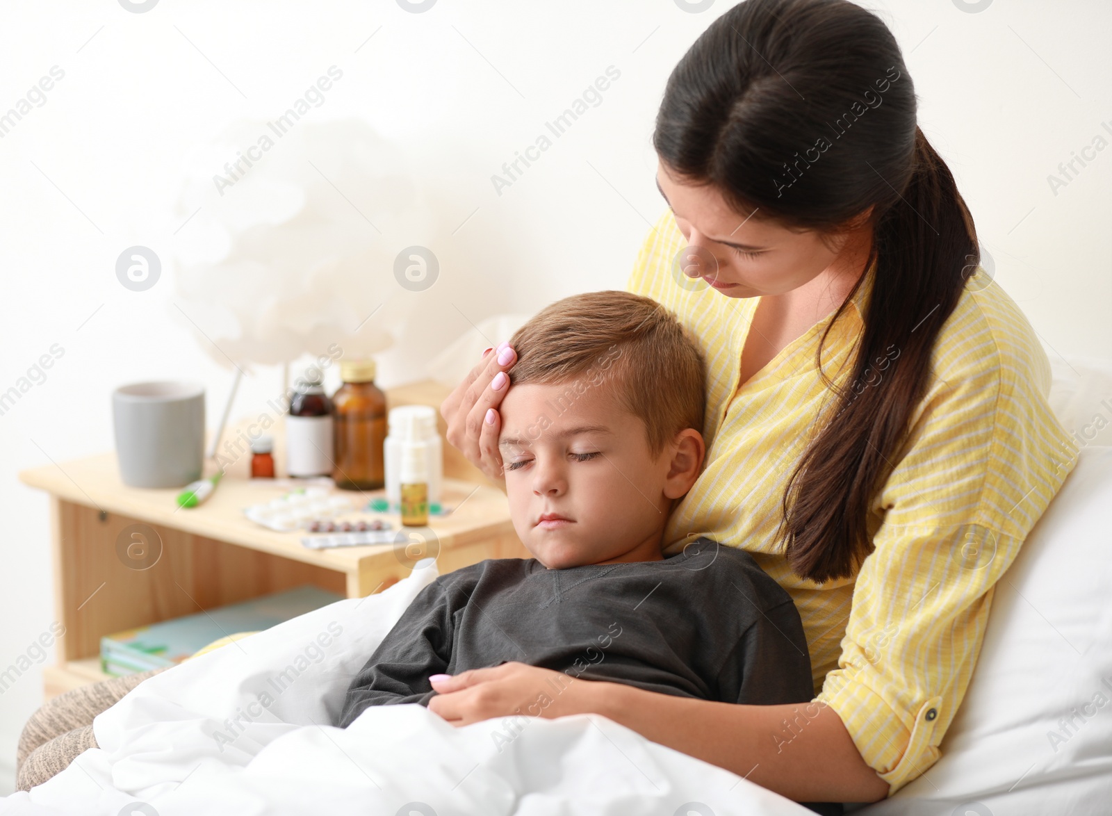 Photo of Mother taking care of her little son suffering from cold in bed