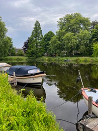 Photo of Beautiful view of city canal with moored boats surrounded by greenery