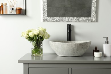 Vase with beautiful white roses and toiletries near sink in bathroom