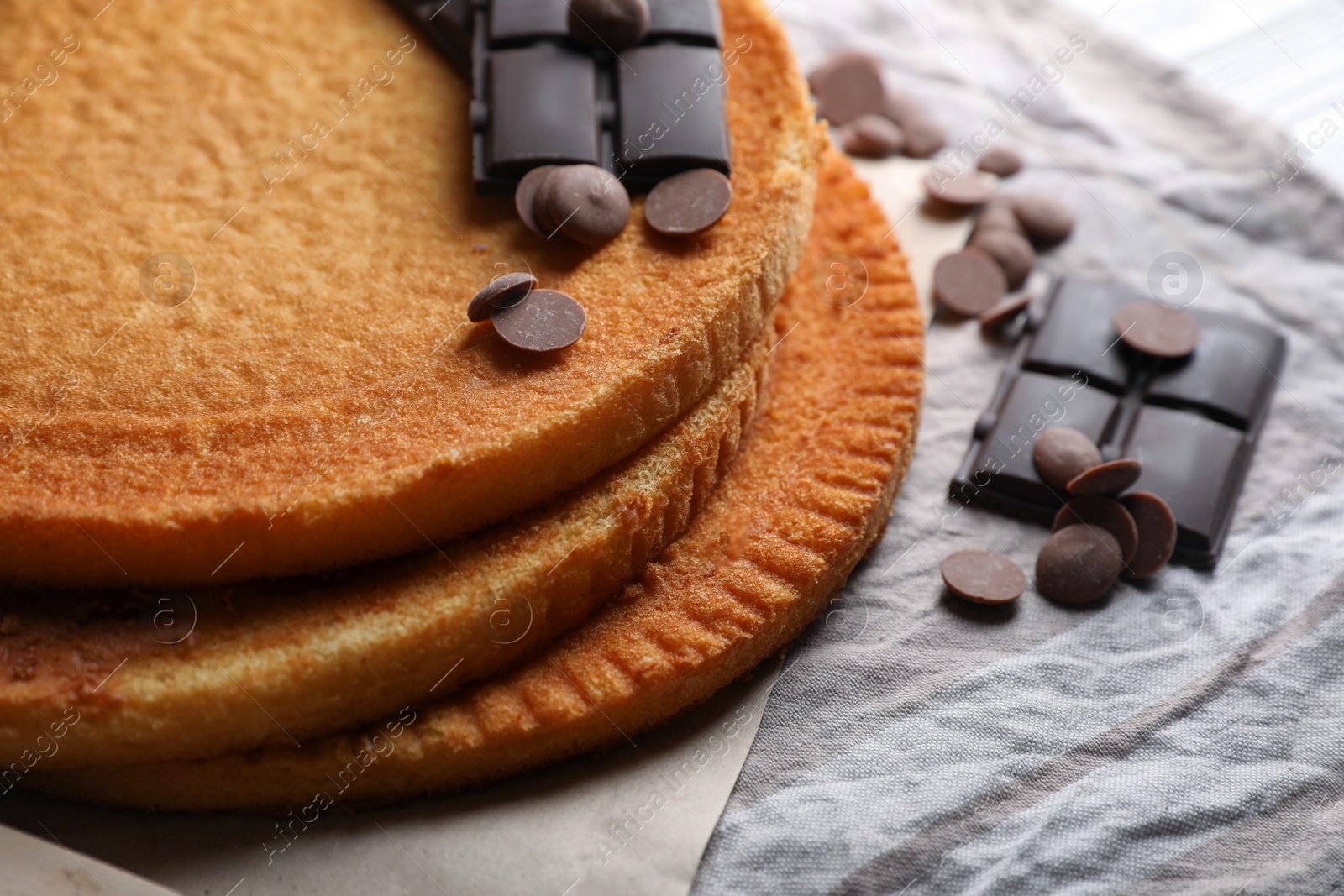 Photo of Delicious homemade sponge cakes and different types of chocolate on grey tablecloth, closeup