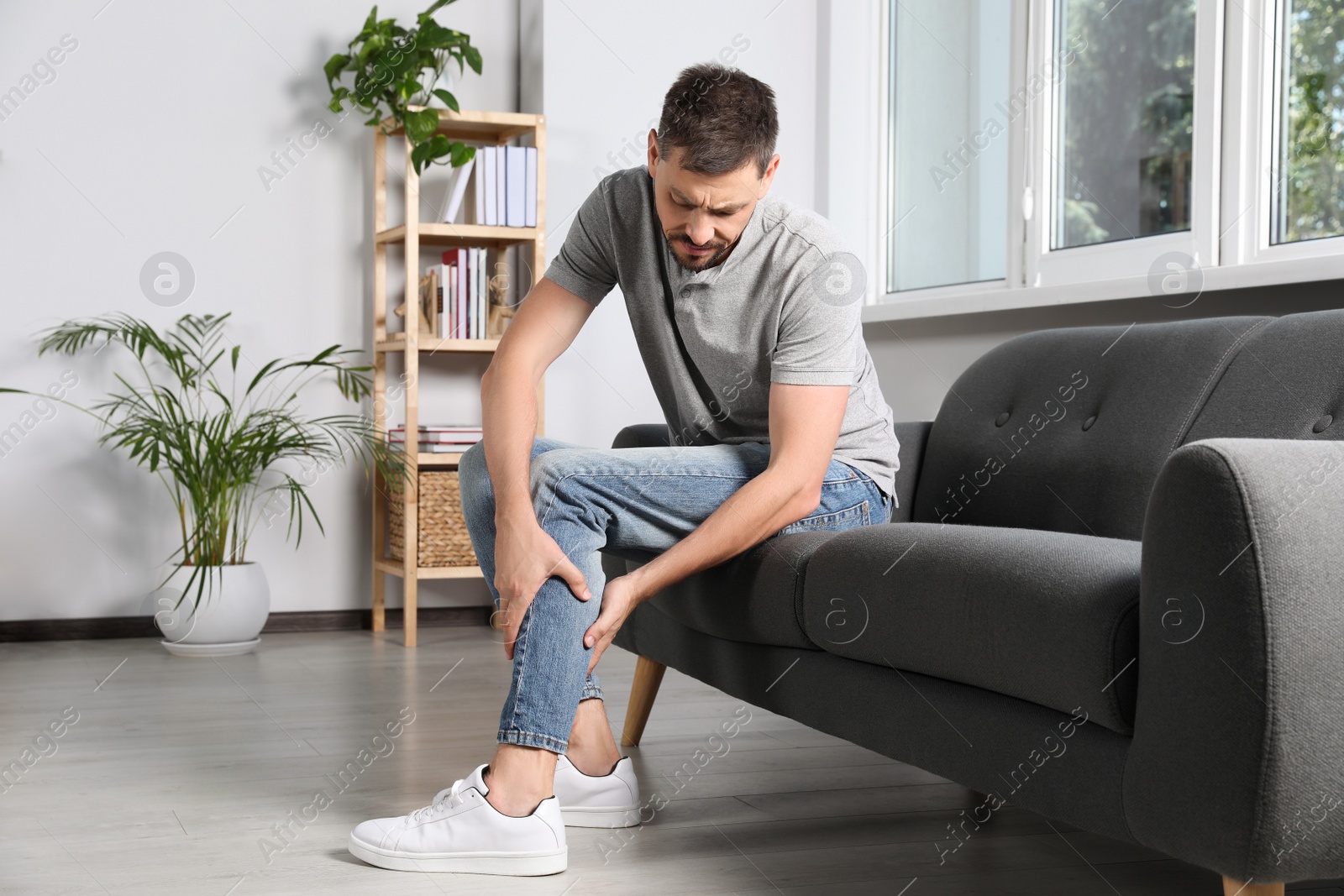 Photo of Man suffering from pain in leg on sofa at home
