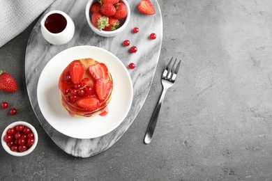 Photo of Tasty pancakes with berries served on grey table, flat lay. Space for text