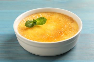 Photo of Delicious creme brulee with mint on light blue wooden table, closeup view