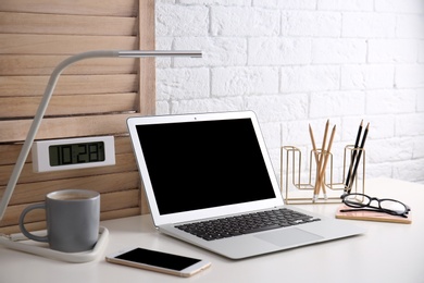 Photo of Modern workplace with laptop on table against brick wall. Mockup for design