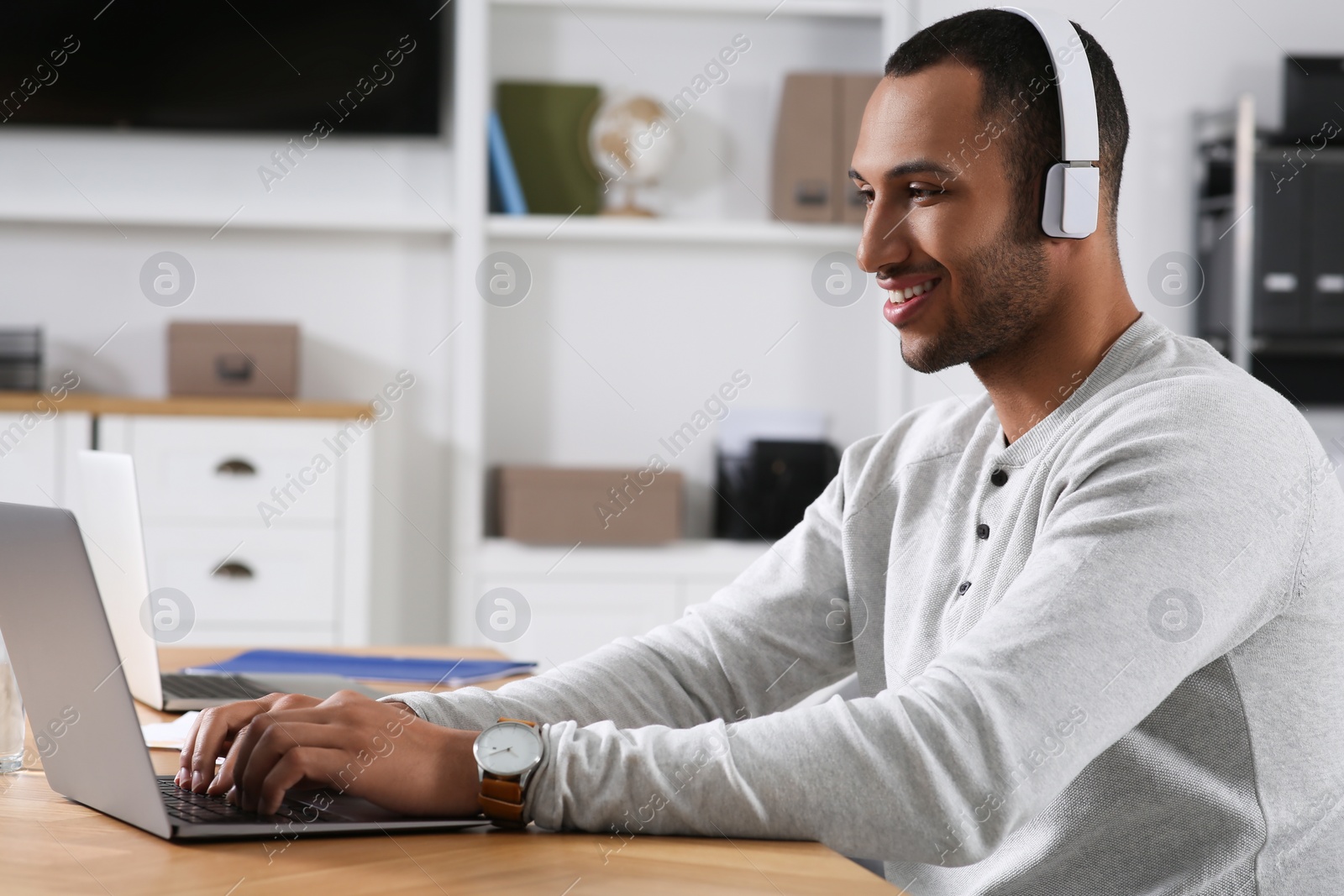 Photo of Young man with headphones working on laptop at table in office