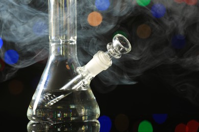 Photo of Closeup view of glass bong with smoke against blurred lights. Smoking device