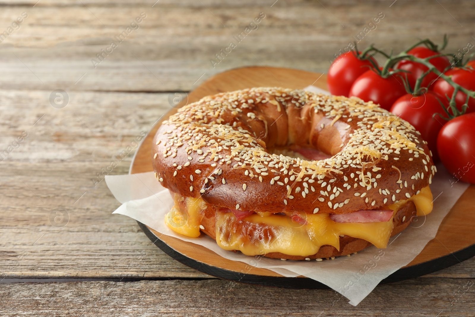 Photo of Delicious bagel with ham, cheese and tomatoes on wooden table, space for text