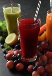 Photo of Delicious colorful juices in glasses and fresh ingredients on black table, closeup