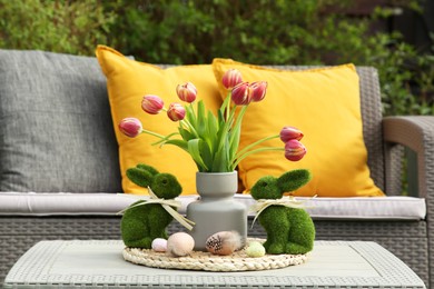 Terrace with Easter decorations. Bouquet of tulips in vase, bunny figures and decorated eggs on table outdoors