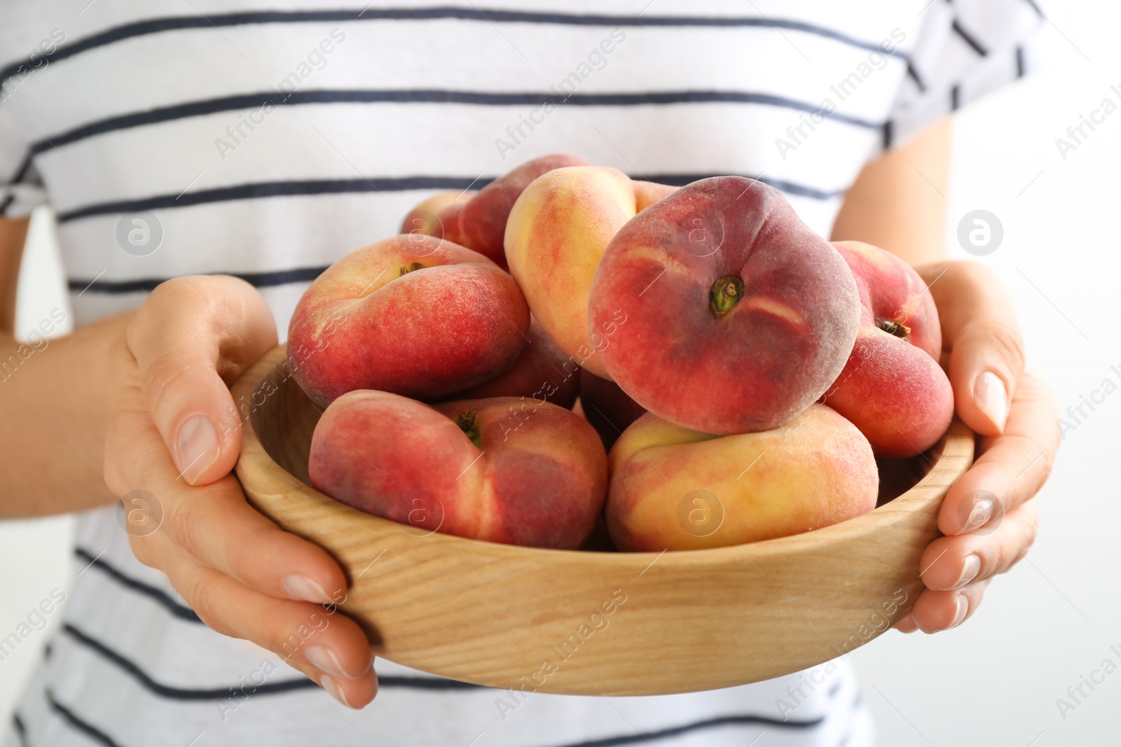 Photo of Woman holding bowl of fresh ripe donut peaches on light background, closeup