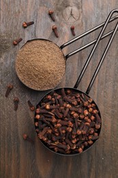 Aromatic clove powder and dried buds in scoops on wooden table, top view