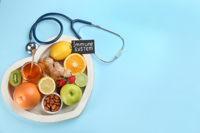 Heart shaped tray of healthy products, stethoscope and card with phrase Immune System on light blue background, flat lay. Space for text