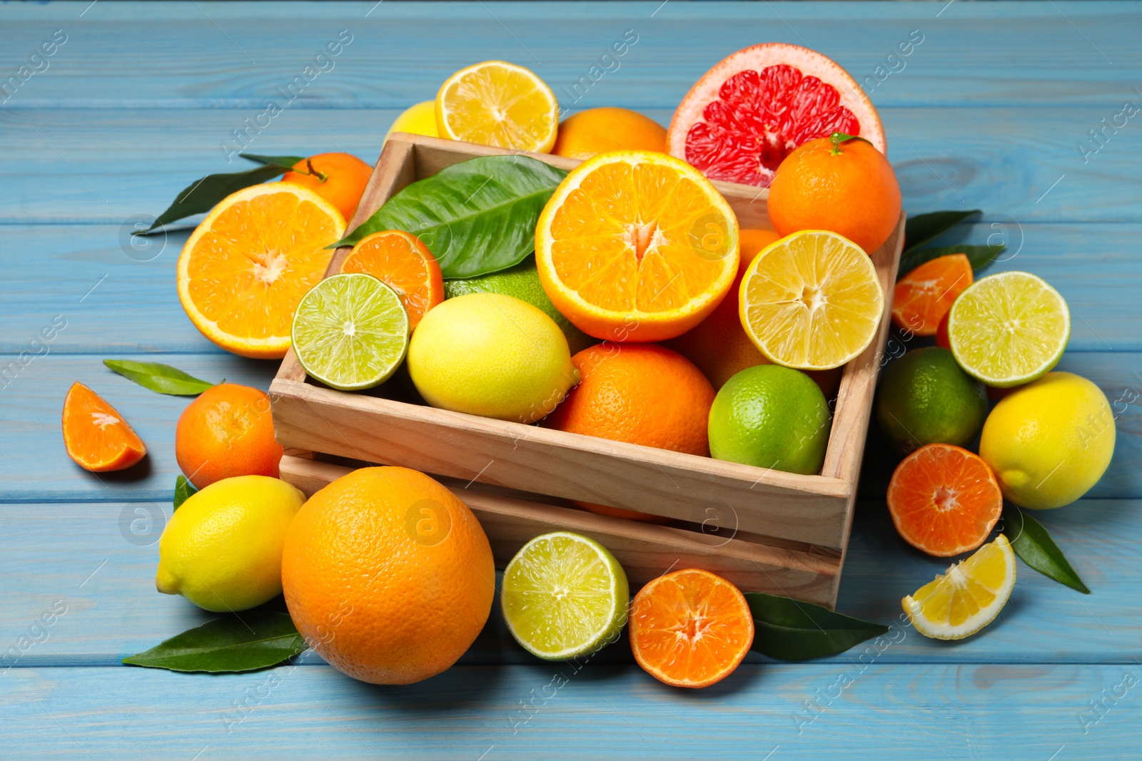 Photo of Different ripe citrus fruits with green leaves on light blue wooden table