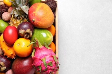 Crate with different exotic fruits on light grey table, top view. Space for text