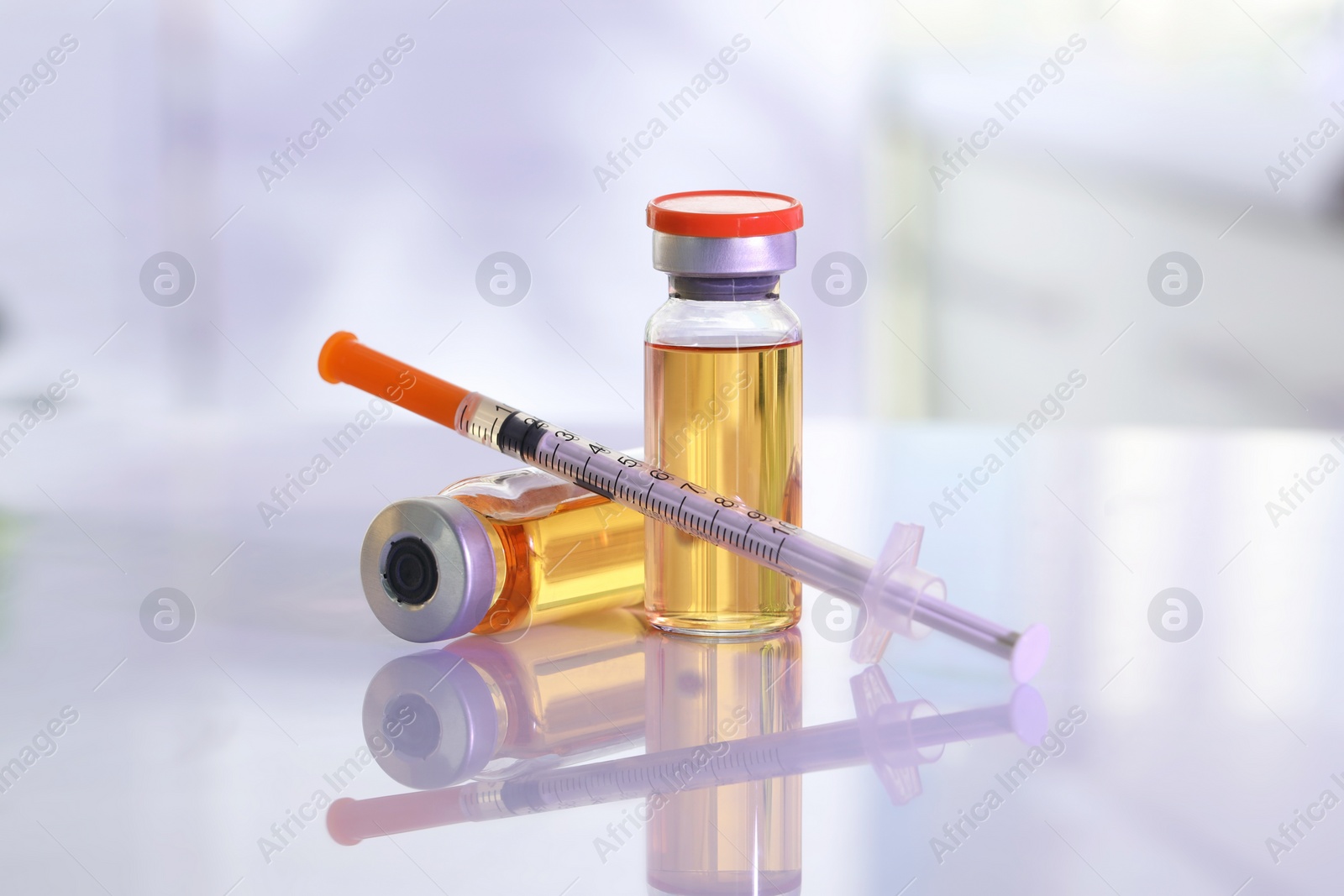 Photo of Glass vials and syringe with orange medication on white table, closeup