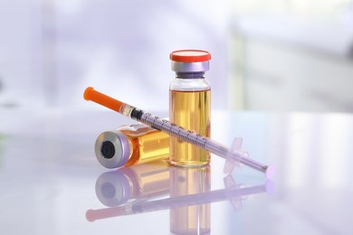 Glass vials and syringe with orange medication on white table, closeup