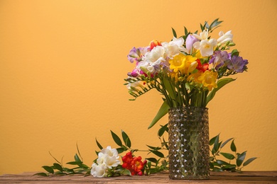 Glass vase with beautiful freesia flowers on table against color background