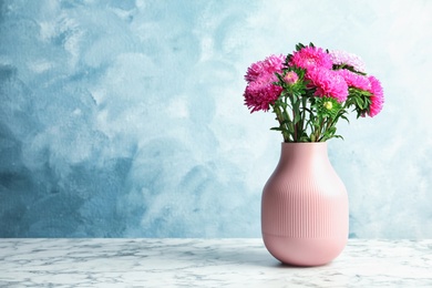 Photo of Vase with beautiful aster flower bouquet on table against color background. Space for text
