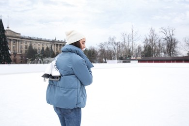 Woman with figure skates near ice rink outdoors. Space for text