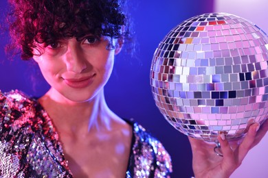 Beautiful young woman with disco ball posing on color background in neon lights, closeup