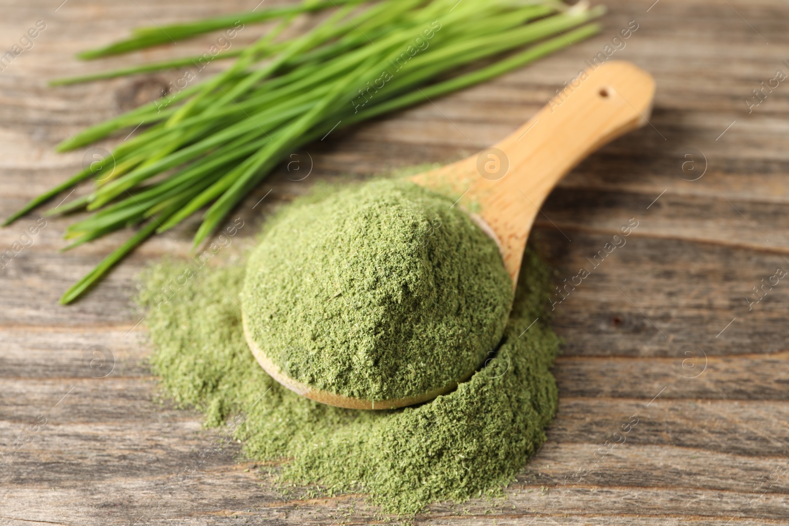 Photo of Wheat grass powder in spoon on wooden table, closeup