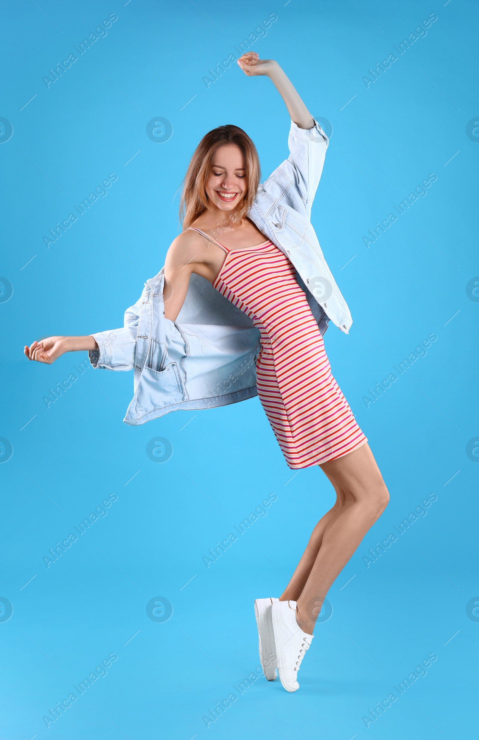 Photo of Beautiful young woman in dress and jacket dancing on blue background