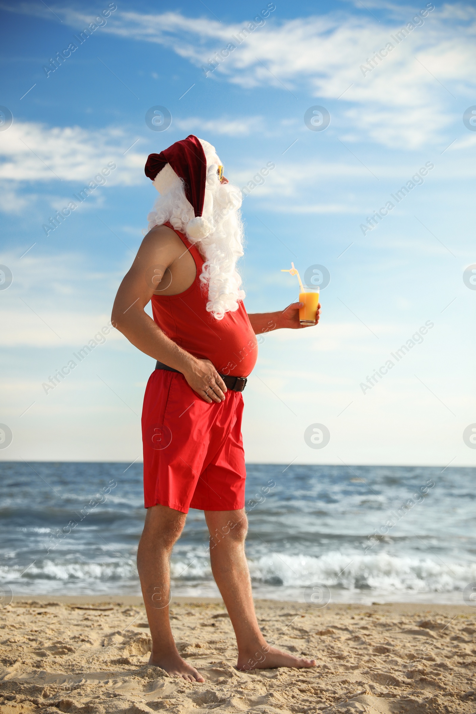 Photo of Santa Claus with cocktail on beach. Christmas vacation