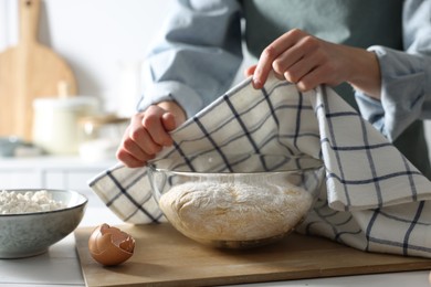 Woman covering dough with napkin at white wooden table in kitchen, closeup