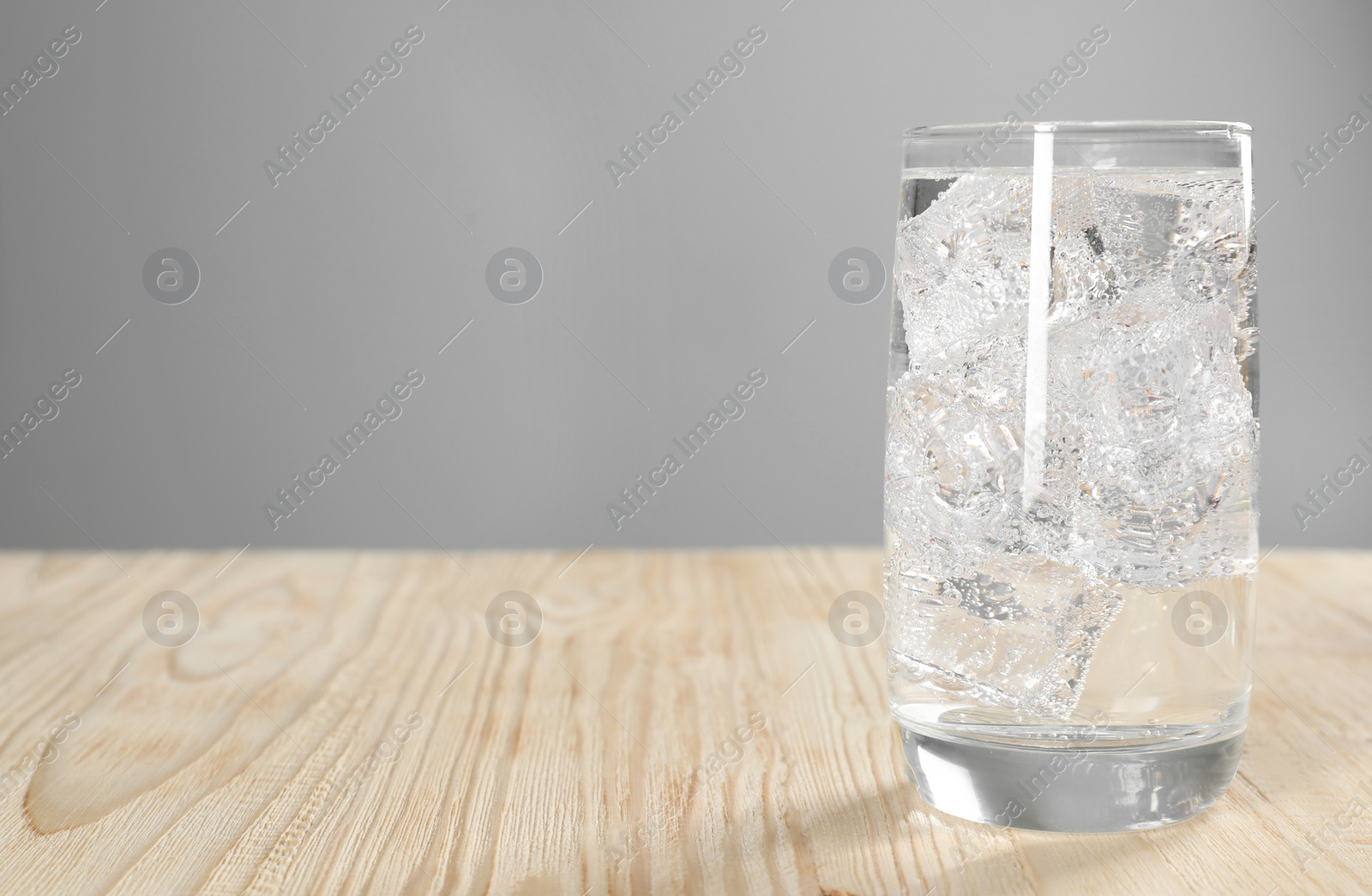 Photo of Glass of refreshing soda water with ice cubes on wooden table, space for text