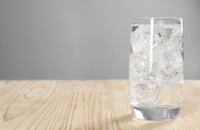 Photo of Glass of refreshing soda water with ice cubes on wooden table, space for text