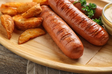Photo of Delicious grilled sausages and fried potatoes on wooden plate, closeup. Barbecue food