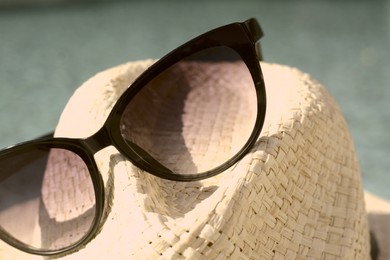 Stylish hat and sunglasses on blurred background, closeup