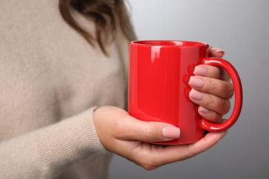 Photo of Woman holding red mug on light gray background, closeup. Mockup for design