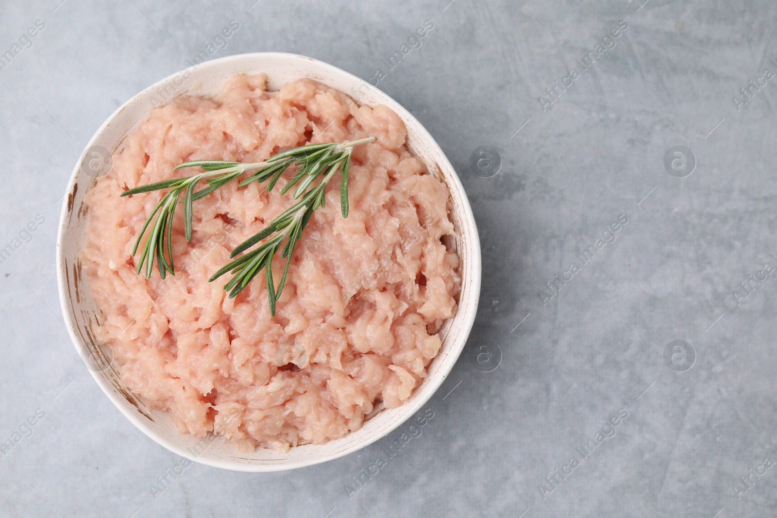 Photo of Fresh raw minced meat and rosemary in bowl on light grey textured table, top view. Space for text