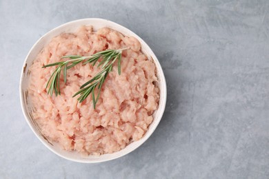 Photo of Fresh raw minced meat and rosemary in bowl on light grey textured table, top view. Space for text