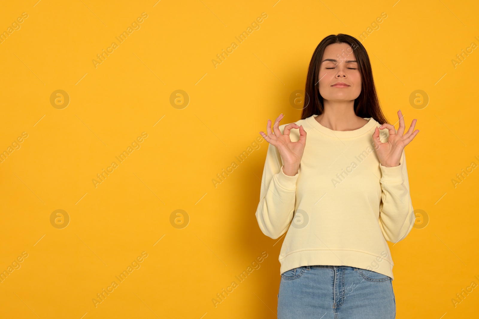 Photo of Young woman meditating on orange background, space for text. Zen concept