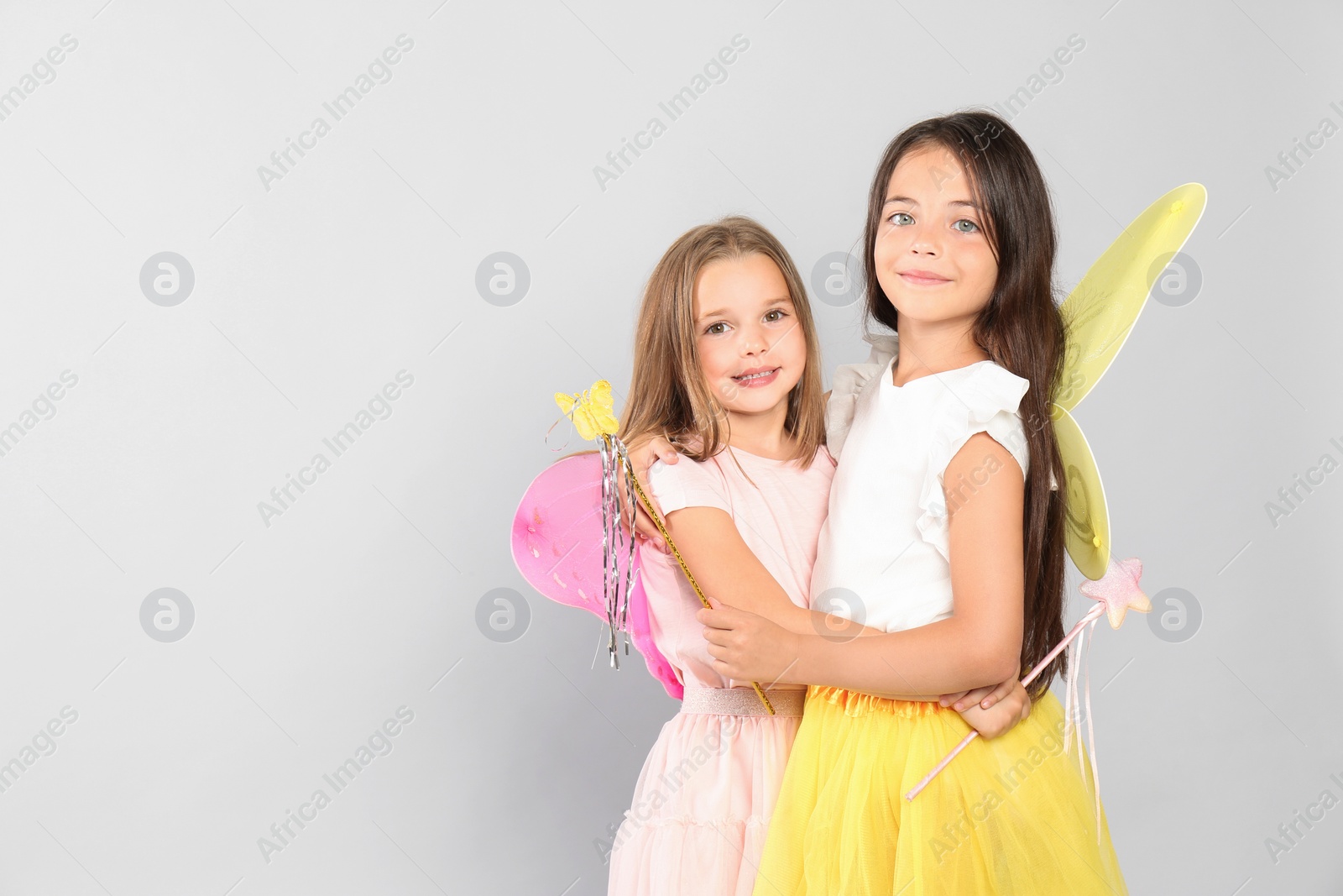 Photo of Cute little girls in fairy costumes with wings and magic wand on light background. Space for text
