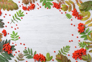 Photo of Frame of fresh ripe rowan berries and green leaves on white wooden table, flat lay. Space for text