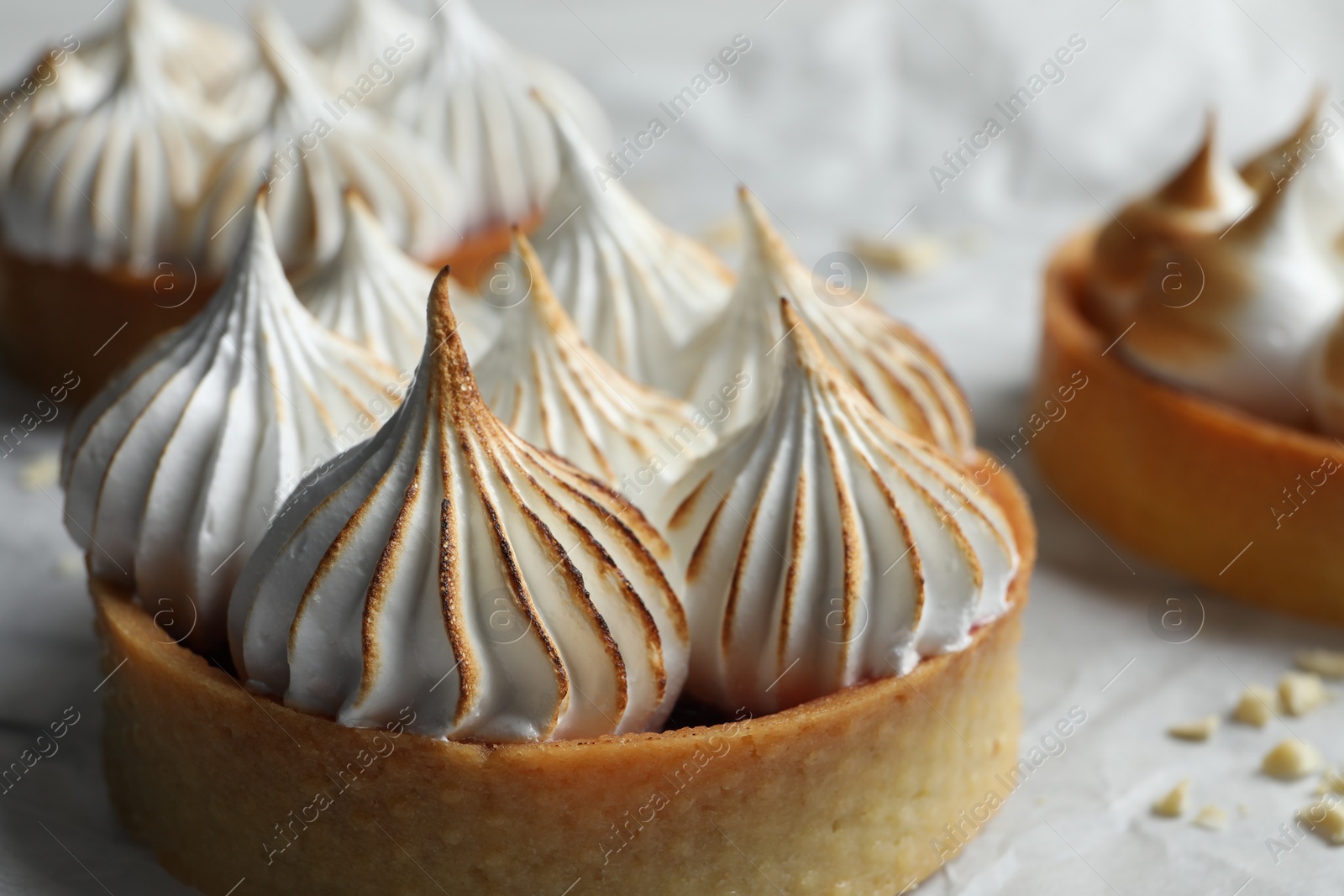 Photo of Tartlets with meringue on parchment paper, closeup. Delicious dessert