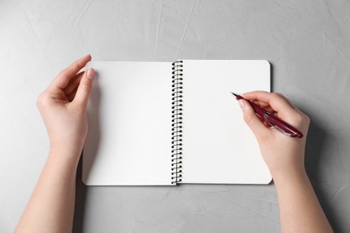 Woman writing in notebook with pen at light grey table, top view