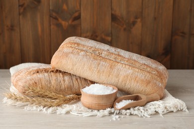 Photo of Fresh crispy ciabattas, salt and spikelets on white wooden table