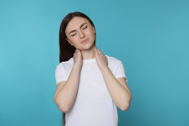 Photo of Young woman suffering from neck pain on light blue background. Arthritis symptoms
